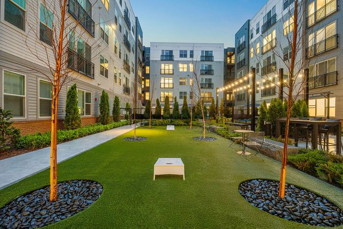 Charming apartment courtyard with lush greenery, modern lighting, and outdoor seating, ideal for relaxation and social gatherings.