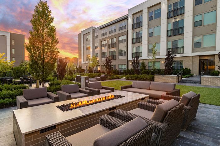 Luxury apartment complex with elegant outdoor seating around a modern fire pit at sunset, surrounded by lush landscaping.
