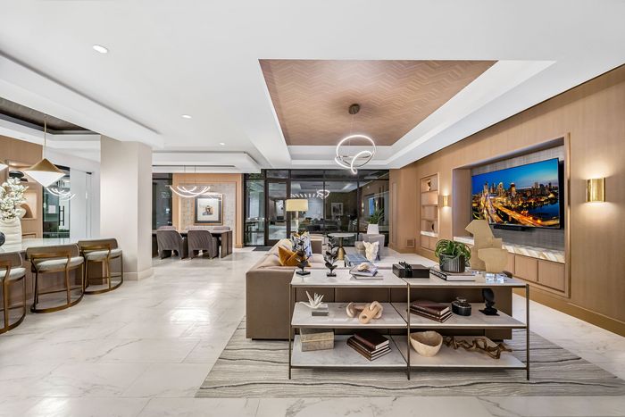 Luxurious open-concept living space featuring a stylish lounge area, elegant dining set, and modern bar stools, complemented by sophisticated lighting and a large wall-mounted TV.