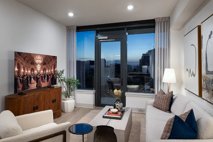 Elegant living room with modern decor, featuring a large flat-screen TV, cozy seating, stylish artwork, and expansive city views through floor-to-ceiling windows.