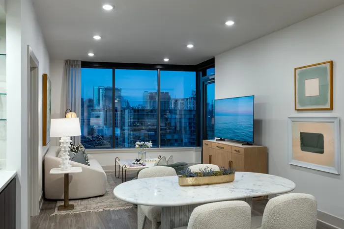 Modern living room with stylish decor, featuring large windows with stunning cityscape views, a cozy sofa, chic dining table, and contemporary art.