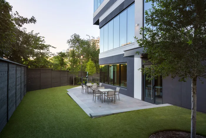 Modern apartment exterior showcasing a sleek design with large windows, a well-maintained patio with outdoor seating, and lush green landscaping.