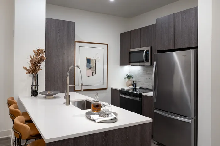 Modern kitchen with sleek dark wood cabinets, elegant white countertops, and stainless steel appliances, perfect for contemporary living.