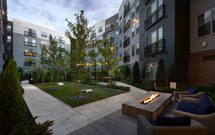 Chic apartment courtyard featuring lush greenery, cozy outdoor seating, modern fire pit, and ambient string lights.