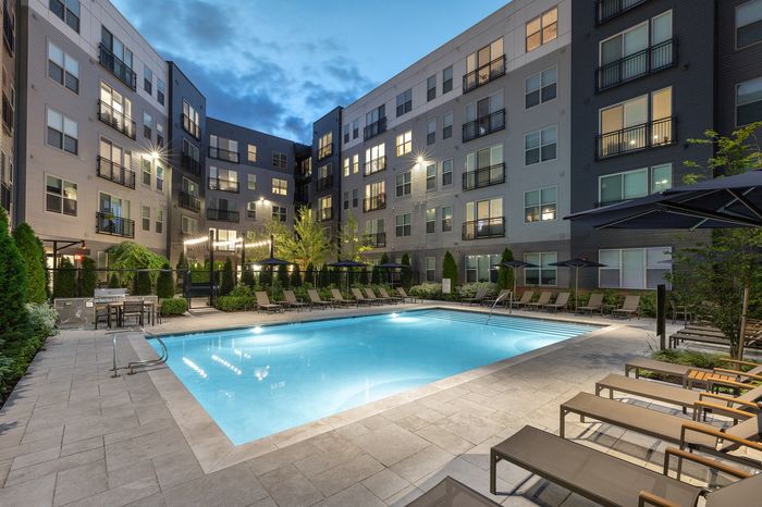 Luxurious apartment complex showcasing a stunning outdoor pool area with modern lounge chairs and lush greenery, perfect for relaxation and leisure.