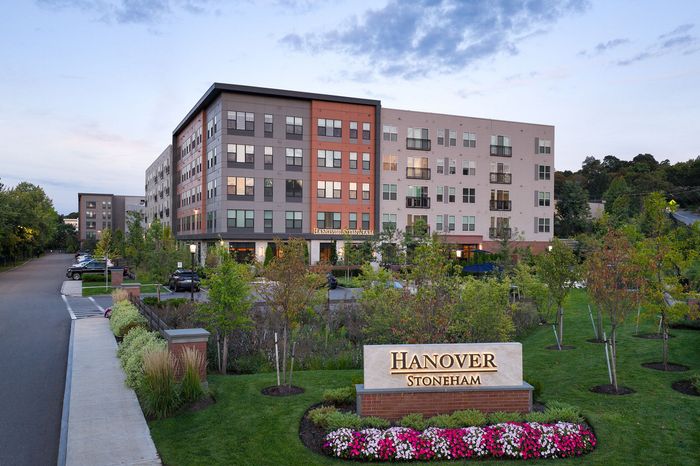 Charming apartment complex at dusk with lush green landscaping, modern architecture, and vibrant flower beds, showcasing tranquil living at Hanover Stoneham.