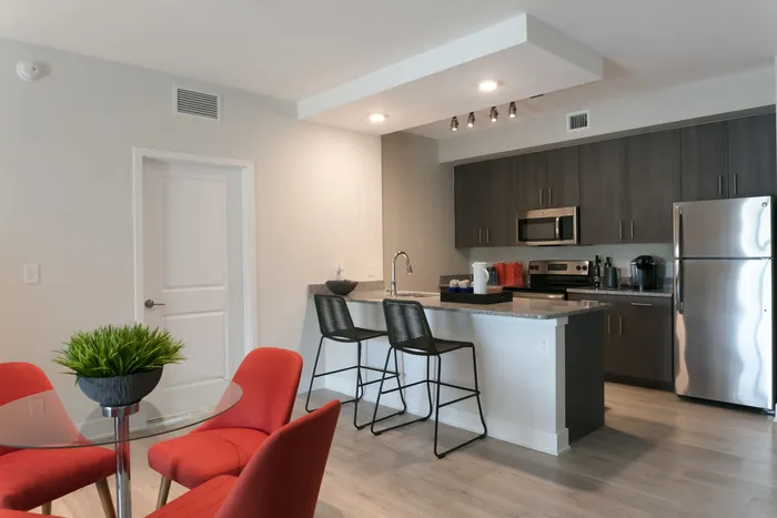 The Reserve at Vero Beach, interior, open concept, kitchen, dining room, large sliding glass doors, ceiling fan, wood floors, stainless steel appliances, refrigerator, microwave, stove/oven, breakfast bar counter, dark cabinets