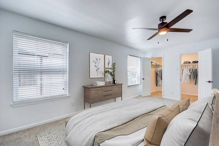 Bright and spacious bedroom at ReNew on Cantrell with soft lighting, featuring a cozy bed, modern ceiling fan, and open walk-in closets.