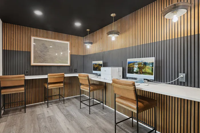 Modern office area with wood paneling, featuring computers and leather chairs in a stylish setting.