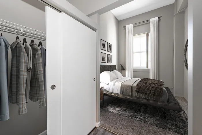 Inviting bedroom with modern design, featuring a neatly organized closet and soft natural light through a large window.