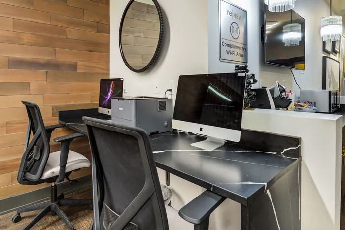 Modern office setup with sleek computers, a printer, and comfortable seating against a stylish wood-panel wall.