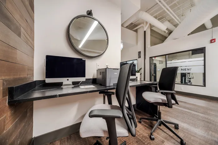 Stylish home office with sleek black desk, modern computer, and round mirror in a contemporary apartment.