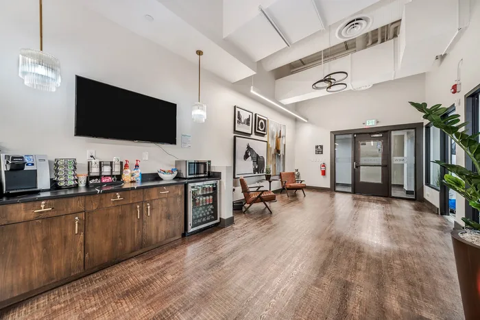 Stylish lounge space featuring wooden flooring, modern seating, a beverage station, and elegant artwork.