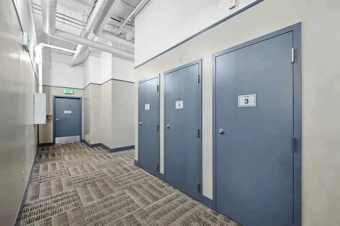 Modern corridor in an apartment building featuring blue numbered doors and industrial ceiling pipes.