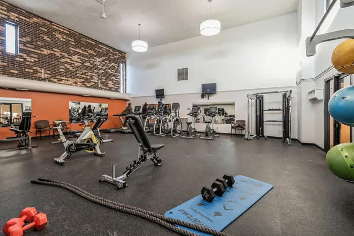 Spacious gym with modern workout equipment, including treadmills, exercise bikes, and free weights, under bright lighting.