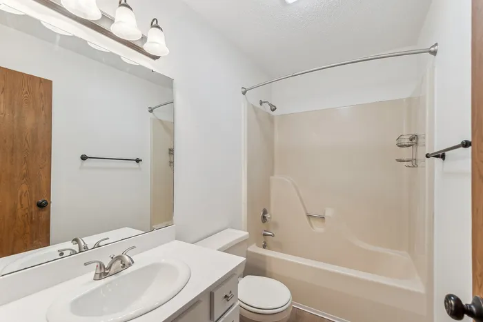 Bright and modern bathroom featuring a clean vanity, large mirror, and a cozy bathtub-shower combo.