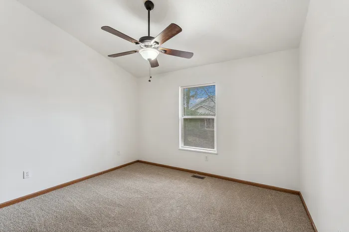 Cozy bedroom interior featuring a ceiling fan, carpeted floor, and a window with natural light.