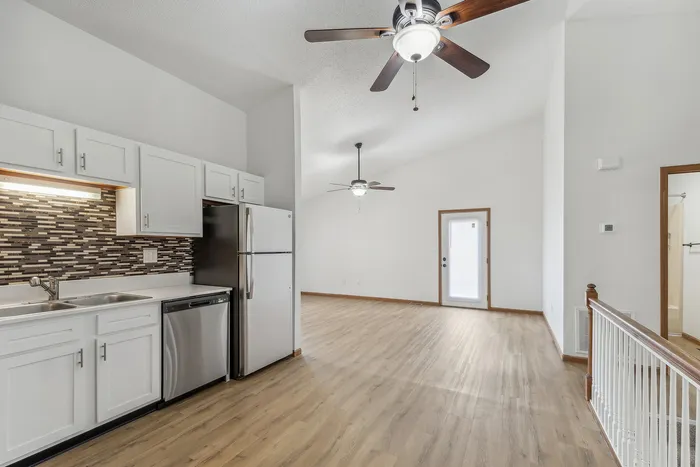 Bright open kitchen with modern cabinets and stainless steel appliances, leading to a spacious living area.