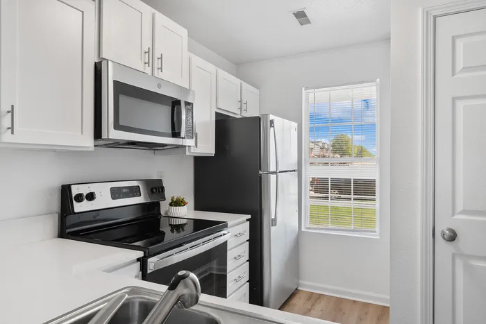 Contemporary kitchen with sleek white cabinets, stainless steel appliances, and a window view.