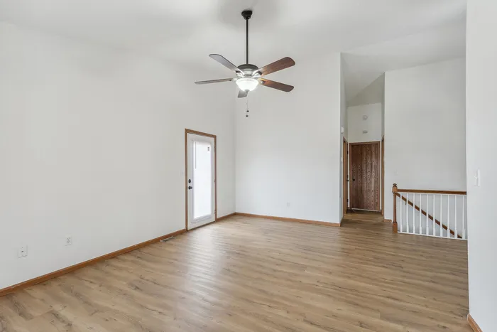 Bright open living room with sleek wooden flooring, ceiling fan, and access to a sunlit porch.
