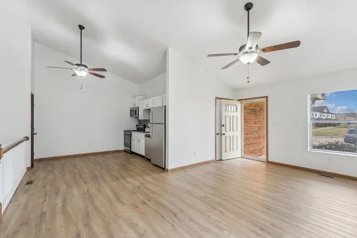 Bright open-concept living space with modern kitchen, large window, and ceiling fans.