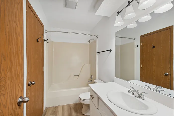 Modern bathroom featuring a sleek vanity, elegant lighting, and a spacious bathtub with wood accents.
