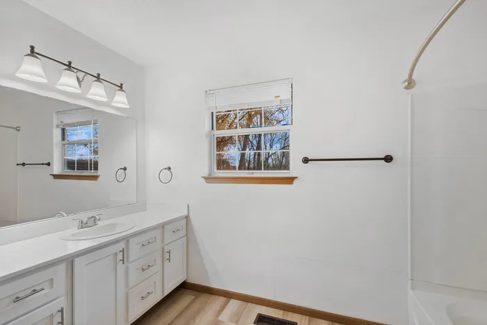 Spacious bathroom with sleek white cabinetry, large mirror, and a window offering natural light.