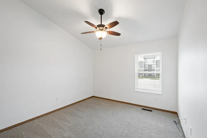 Spacious bedroom with plush carpeting and a ceiling fan, featuring a large window for natural light.