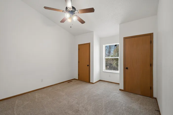Inviting bedroom with plush carpet, ceiling fan, and ample natural light from a window.