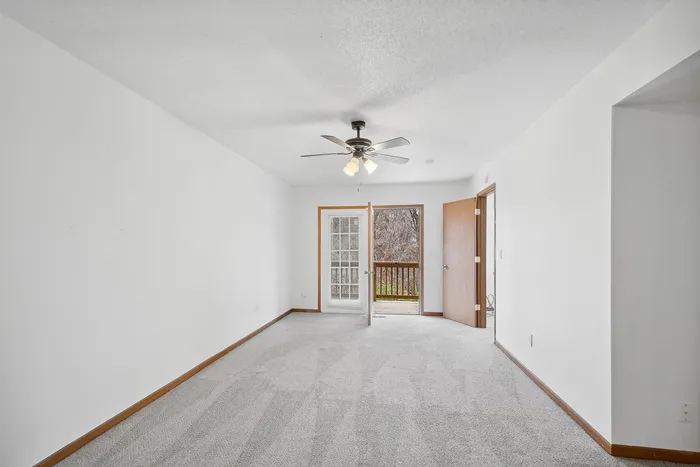 Spacious living room with carpeted floors, ceiling fan, and double doors leading to a balcony view.