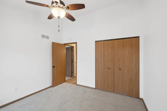 Bright and airy bedroom with ceiling fan, wood closet doors, and plush carpet flooring.