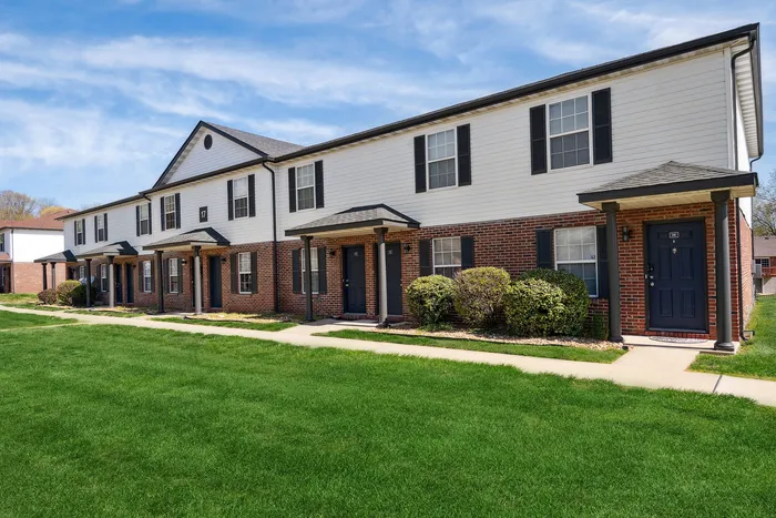 Charming row of modern townhouses with brick exteriors, lush green lawns, and clear blue skies.