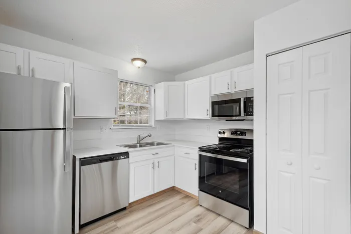 Contemporary kitchen with stainless steel appliances, white cabinetry, and hardwood flooring.