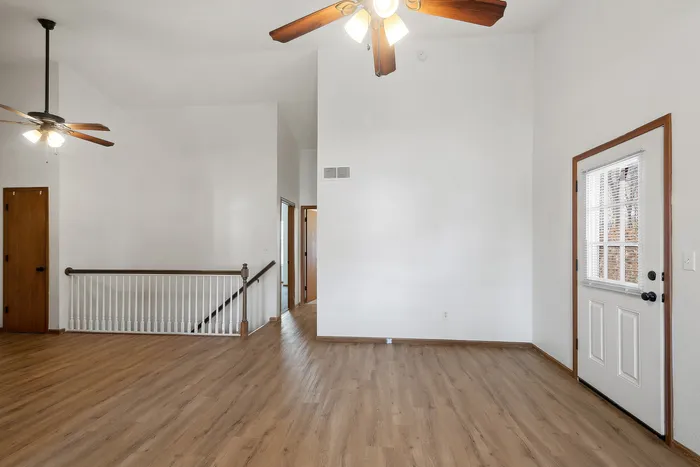 Bright open living space with wooden floors, ceiling fans, and a staircase entry.