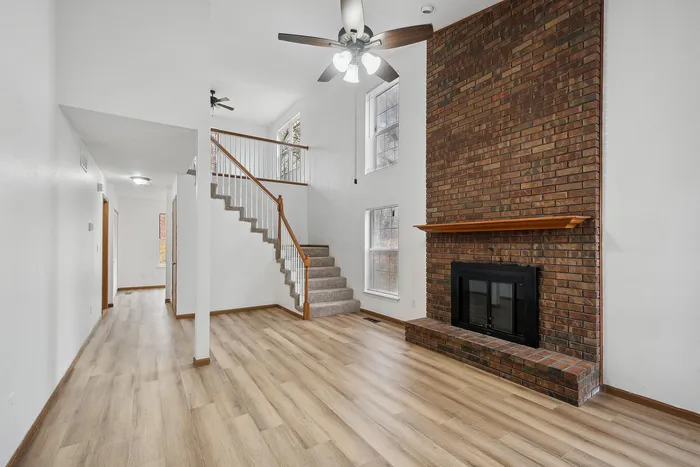 Spacious living area with a rustic brick fireplace, wooden flooring, and a stylish staircase.