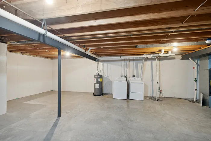 Bright, open basement featuring laundry appliances and water heater with exposed ceiling beams.