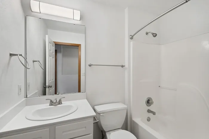 Contemporary bathroom featuring a sleek white vanity, large mirror, and shower-tub combo.