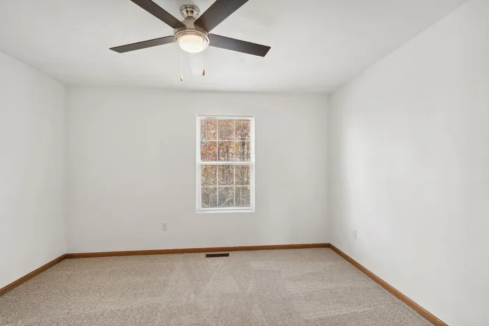 Well-lit empty room with a ceiling fan and large window.