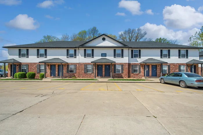 Charming two-story apartment complex with brick and white siding, featuring neat landscaping and paved parking.