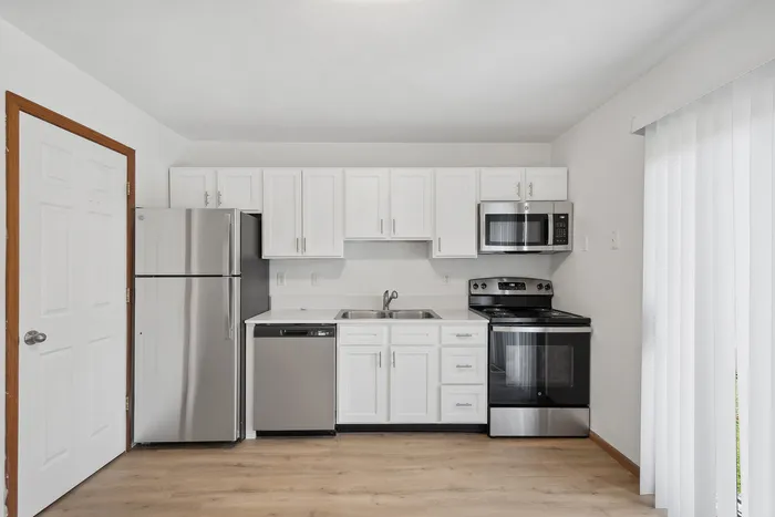 Contemporary kitchen with stainless steel appliances, white cabinetry, and wooden flooring.