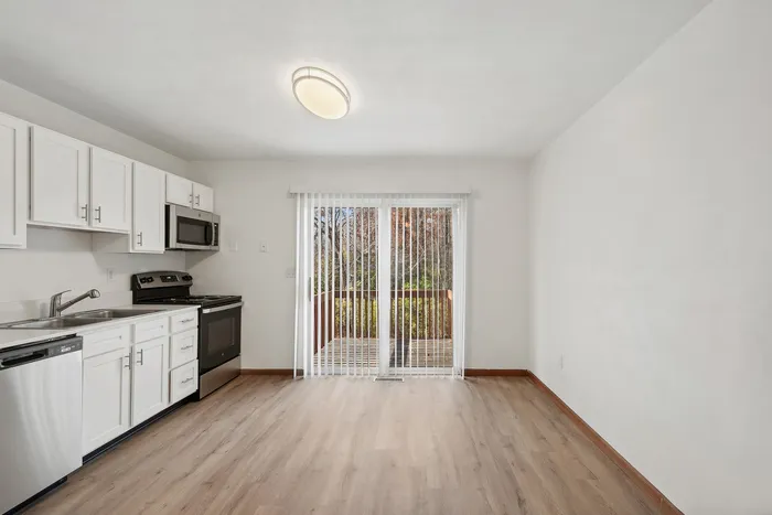 Modern kitchen with white cabinets and stainless steel appliances next to a dining area with sliding glass doors.