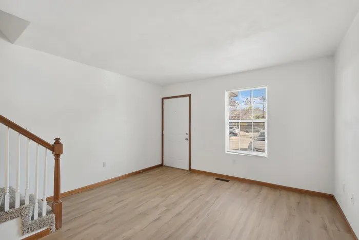 Inviting, sunlit entryway featuring elegant hardwood floors and a wooden staircase.