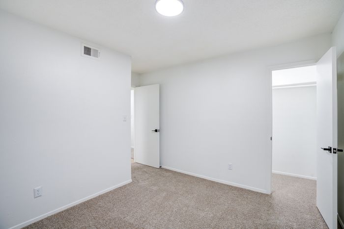 Spacious white-walled bedroom with soft carpet and modern doors, illuminated by a central ceiling light.