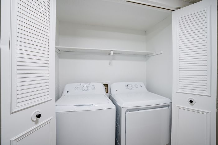 Compact laundry area with modern washer and dryer inside a closet with louvered doors.