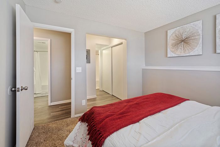 ReNew Foothills Inviting bedroom featuring a comfortable bed with a red throw and modern wall art, adjacent to a bathroom and hallway.