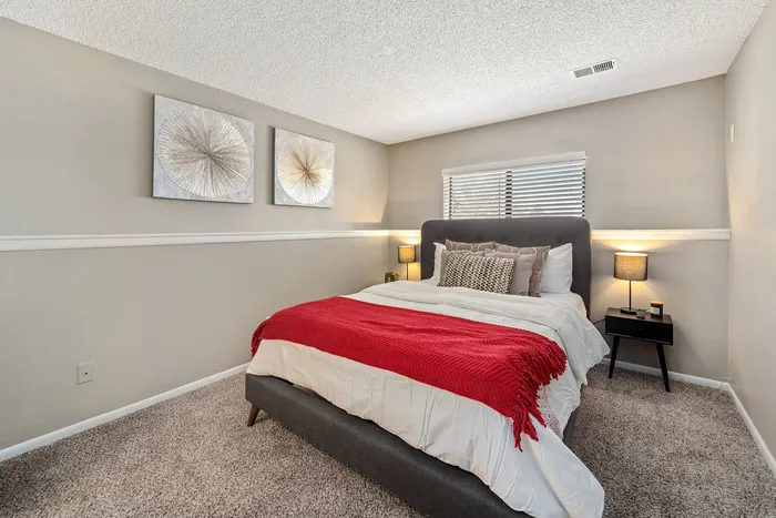 ReNew Foothills Inviting bedroom with a plush bed, red throw, soft lighting, and elegant wall art.