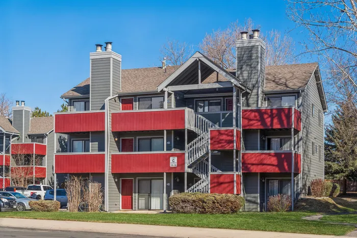 ReNew Foothills Impressive multi-story apartment building with vibrant red balconies and a gray fa&ccedil;ade under a clear blue sky.