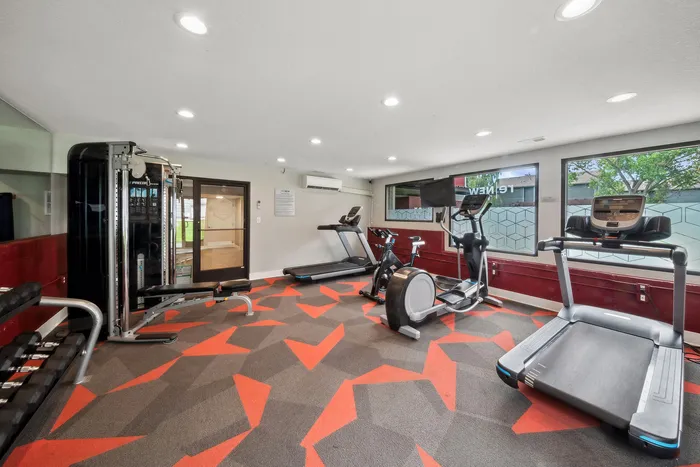 ReNew Foothills Well-equipped apartment gym with cardio machines and a weight station on a vibrant geometric carpet.
