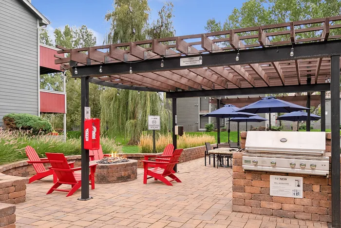 ReNew Foothills Charming outdoor lounge with pergola, fire pit, red chairs, and a modern grill amidst lush greenery.