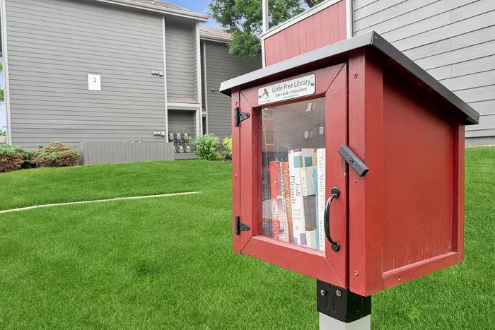 ReNew Foothills Charming little free library set in a lush green community lawn with a backdrop of modern buildings.